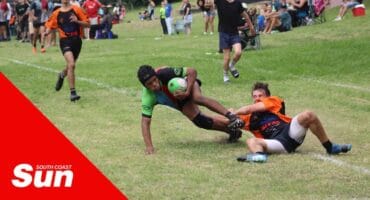 Two rugby players on the field tussling for the ball.