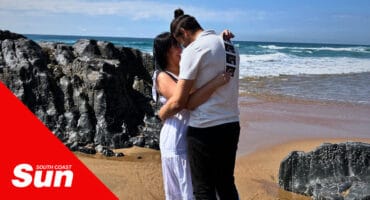 a man and woman holding one another on the beach, also holding pregnancy scans