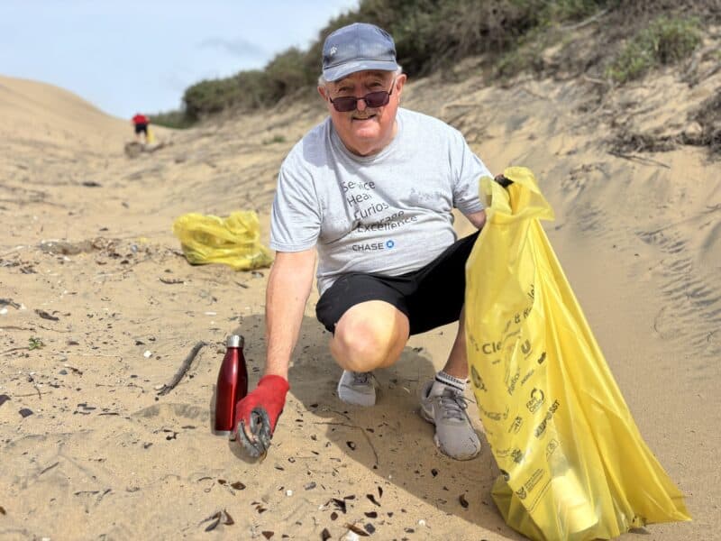a man holding a recycling bag and picking up litter on the beach