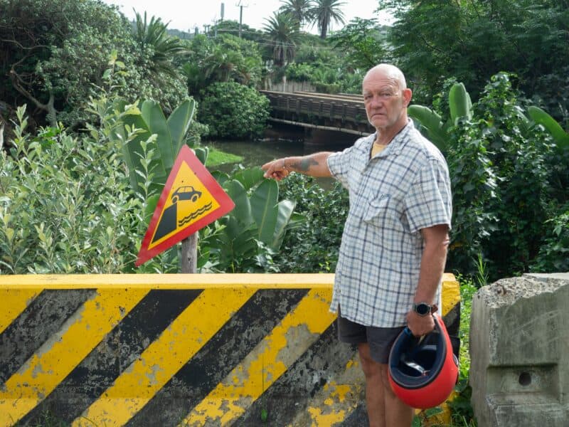 a man gesturing towards a road sign in front of a bollard