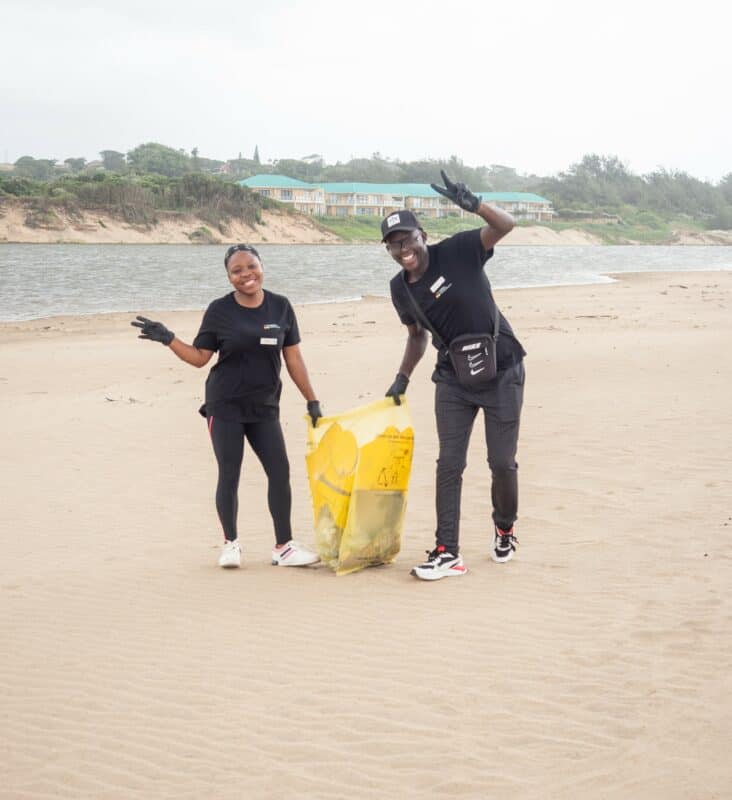 a woman and a man smiling and holding a bag of litter on the beach