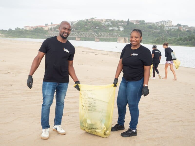 a woman and a man smiling and holding a bag of litter on the beach