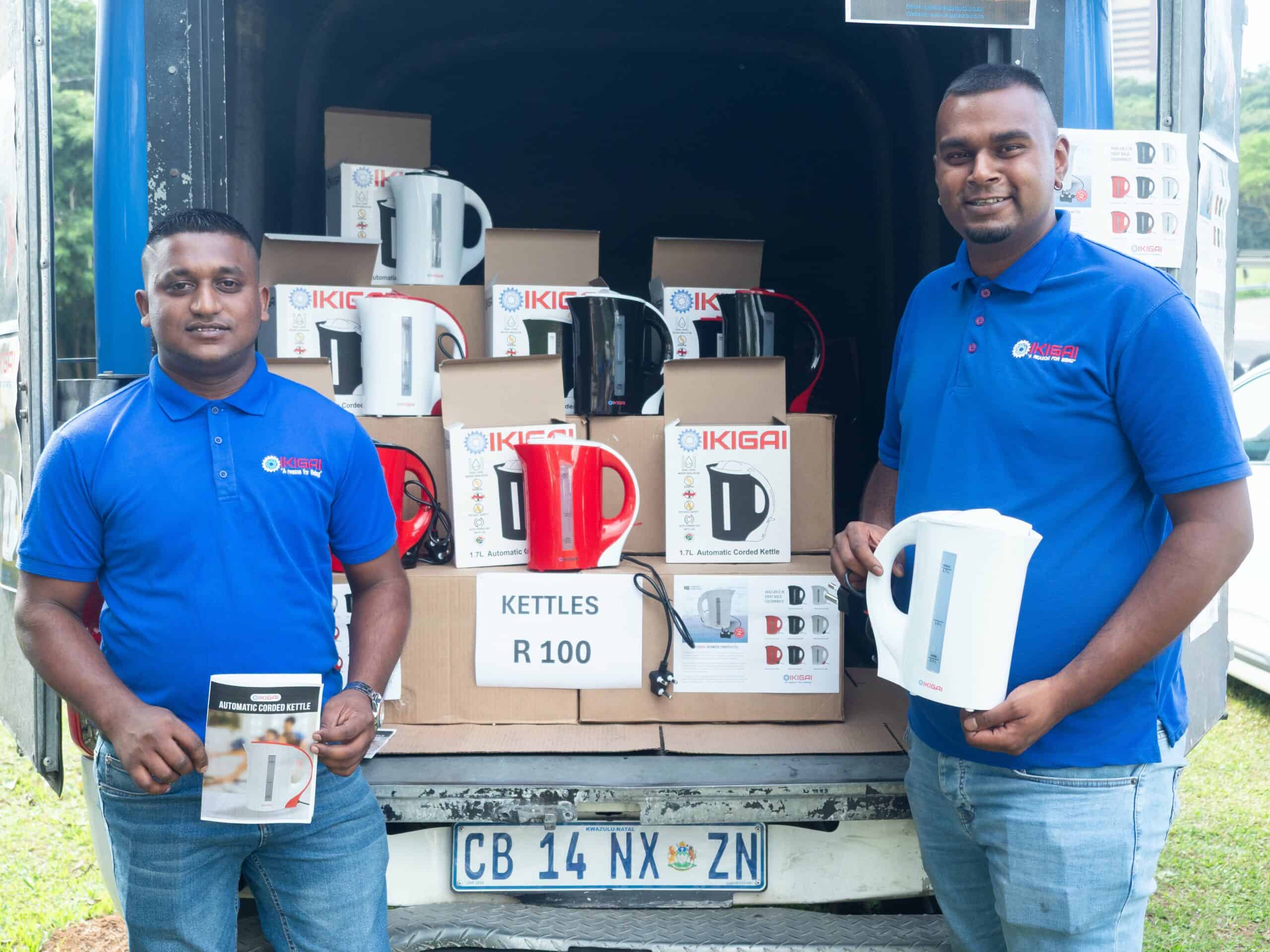 two men outside the back of a truck full of kettles, holding a kettle