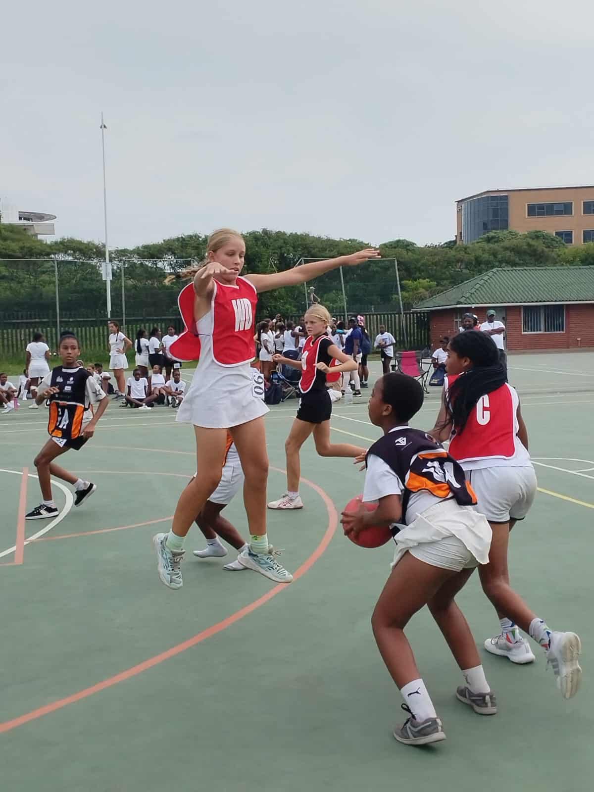 a netball match on a court, a player jumping in the air to body block a pass