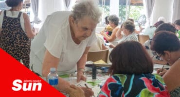 an art class, with the elderly art teacher demonstrating hands-on to a student technique
