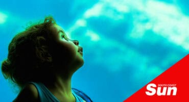 a photograph shot through aquarium glass with a child looking up at the fish