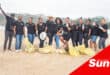 a big group of workers on a beach with collected bags of litter
