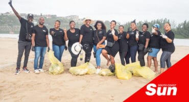 a big group of workers on a beach with collected bags of litter