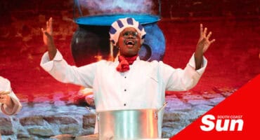 an actor playing a chef in a kitchen with his arms gesturing upward