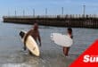 two surfers at the beach, knee-deep in water holding their surfboards