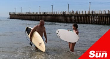 two surfers at the beach, knee-deep in water holding their surfboards