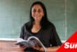 a teacher holding her textbook stood in front of a chalkboard