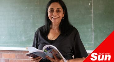 a teacher holding her textbook stood in front of a chalkboard