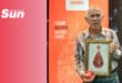 a man in front of a blood donation service sign, holding a certificate and gift