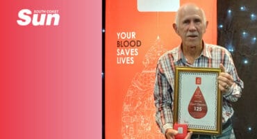 a man in front of a blood donation service sign, holding a certificate and gift