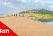 a beach, community members digging the sand to breach the river