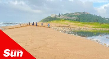 a beach, community members digging the sand to breach the river