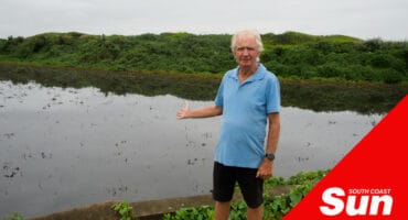 a man standing on a river bank gesturing towards the filth inside the water