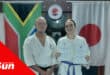 two karate fighters standing in a dojo, south african and japanese national flags in the background.