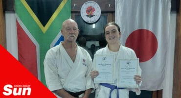 two karate fighters standing in a dojo, south african and japanese national flags in the background.