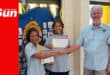 a young woman is handed a certificate of induction by two club members