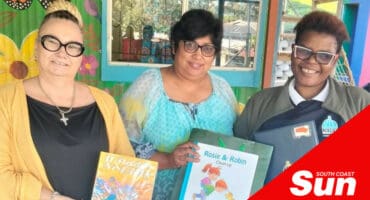 three woman holding books in front of a crate building