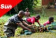 multiple young men in Kariba weed infested waters, pushing netted weeds out of the water