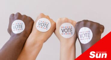 multiple hands and forearms of different complexions with voting stickers on the top