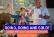a woman holds up an item up for auction and an auctioneer points to a bidder
