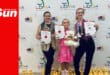 three dancers, young and old, show off their certificates, trophies and awards in front of a banner