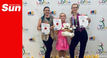 three dancers, young and old, show off their certificates, trophies and awards in front of a banner