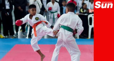 Two young martial arts fighters spar on a tatami with crowds of spectators watching