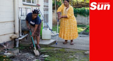 a woman shoveling sewage outfall away from a property's backyard while a woman using crutches watches