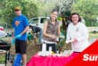 a photograph of three people manning a car boot market stand, two making a hot dog, one working a grill