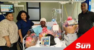 people handing over a get well soon hamper to a hospital patient who has a head bandage on.