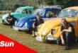 three old Volkswagen Beetles with the three drivers crouched in front of each one