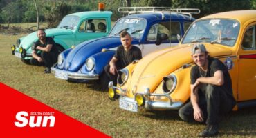 three old Volkswagen Beetles with the three drivers crouched in front of each one