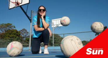 a woman crouches down at a netball field with netballs bouncing all around her