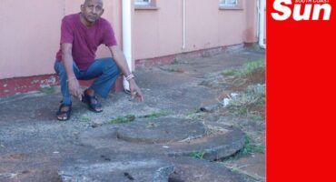 a man pointing at manholes outside a flat building