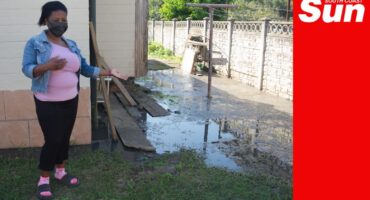a woman with a mask points out sewage overflow in the backyard of a residence