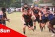 a rugby player holds onto the ball and runs past defenders on a field