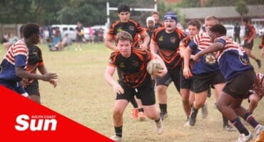 a rugby player holds onto the ball and runs past defenders on a field