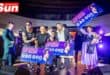 a group photograph on a concert stage with people holding giant cheques and celebrating