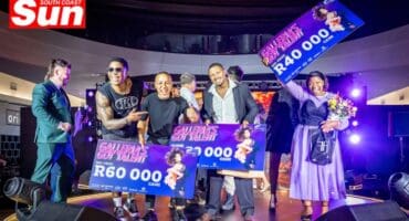 a group photograph on a concert stage with people holding giant cheques and celebrating