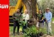 a group photograph with people holding up plants next to a tree