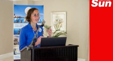 a person standing behind a podium with a mic and a banner behind her