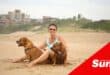 a woman sitting on the beach with her two dogs