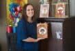 a woman holds her book release next to a book shelf