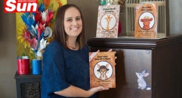 a woman holds her book release next to a book shelf