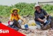 two woman sat on the beach filling refuse bags